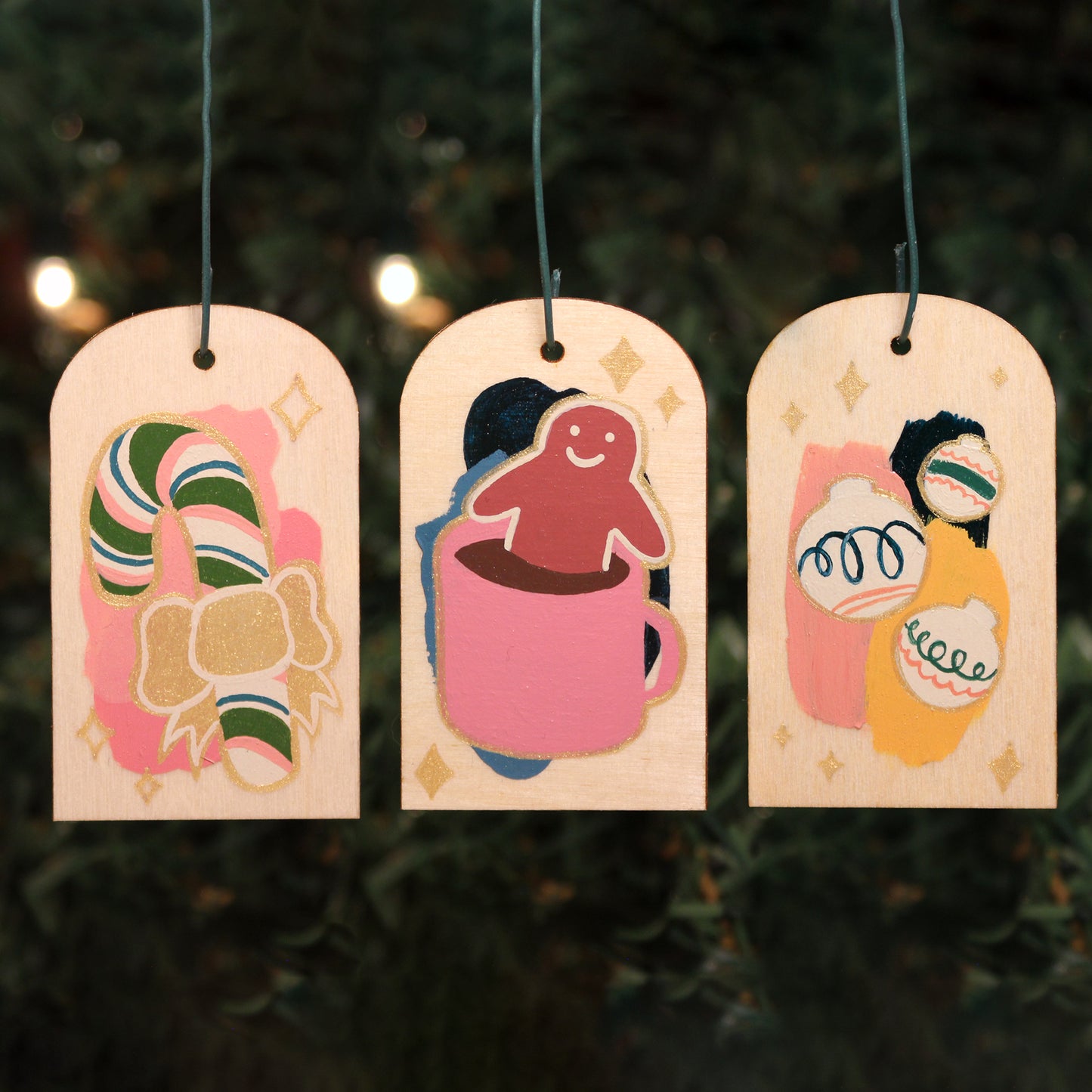 Three Christmas wooden ornaments hang in front of lit up evergreens.