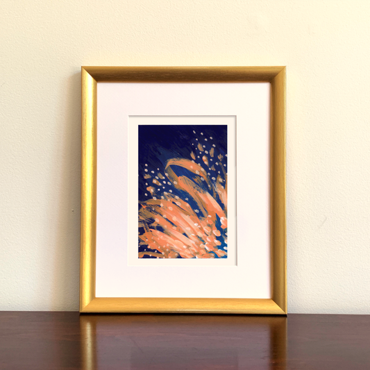 Framed abstract artwork with orange and blue colors on a beige wall.