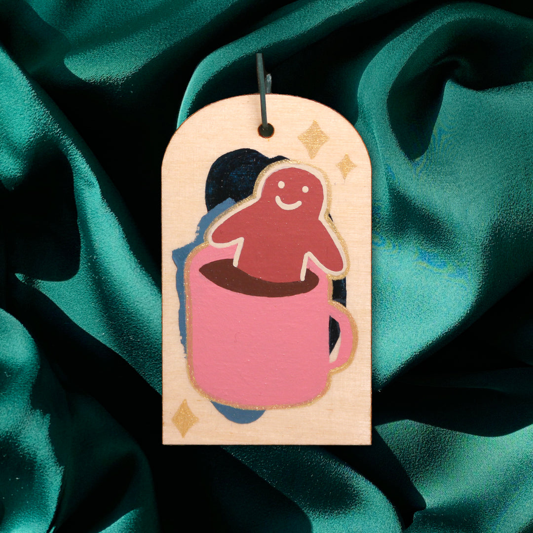 Hand-painted wooden ornament of a gingerbread man with a pink hot chocolate tub-mug, hanging from a hook.