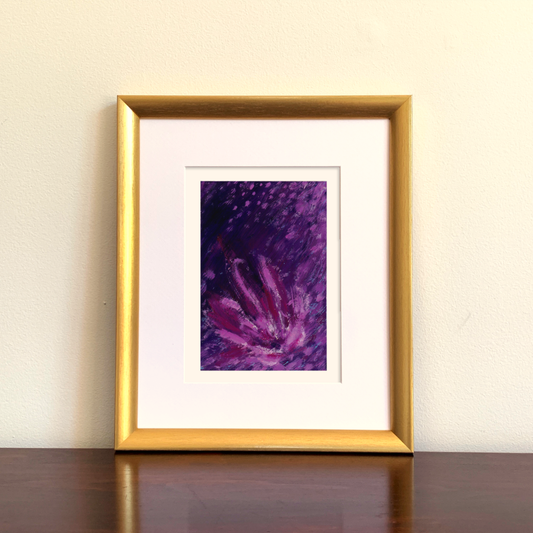 Framed abstract art print with purple and pink hues on a beige wall.