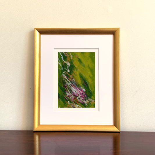 Framed abstract artwork with green and purple, magenta tones on a beige wall.