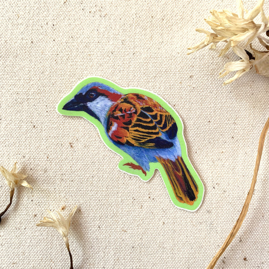 Colorful bird-shaped sticker on a textured beige background with dried flowers.