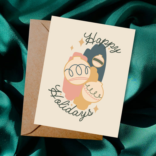 Greeting card and envelope with ornament illustration and 'Happy Holidays' text on a dark background.