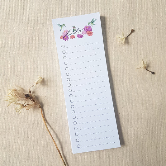 Hummingbird to do list notepad on fabric surface surrounded by dried flowers.